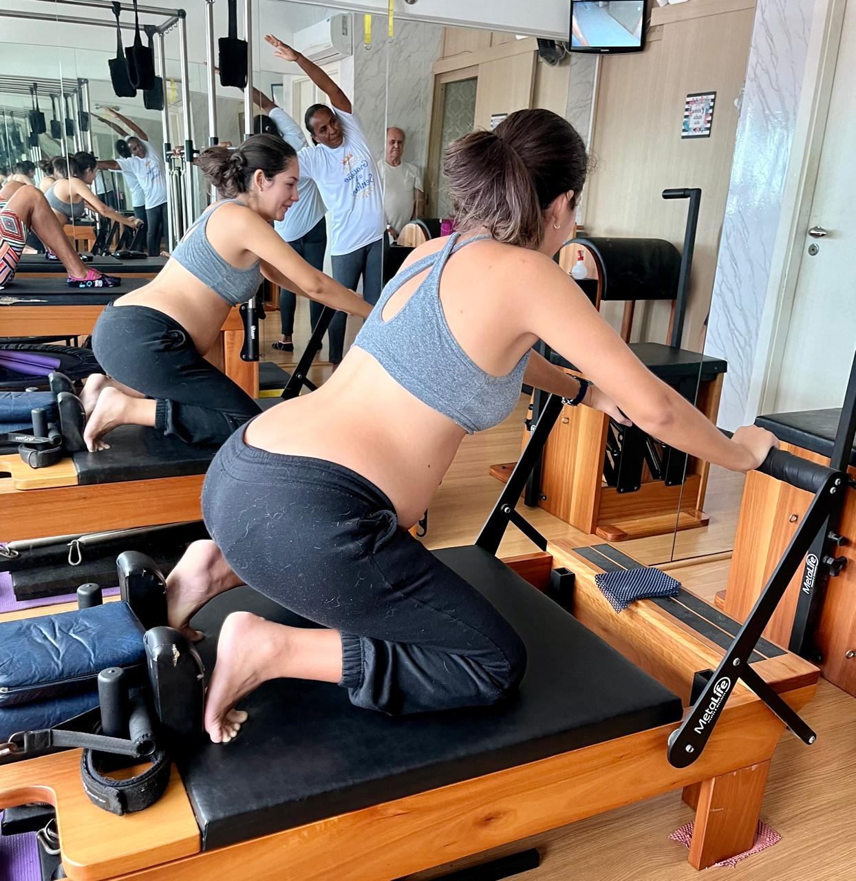 Gestante realizando exercício de Pilates no Reformer com acompanhamento profissional